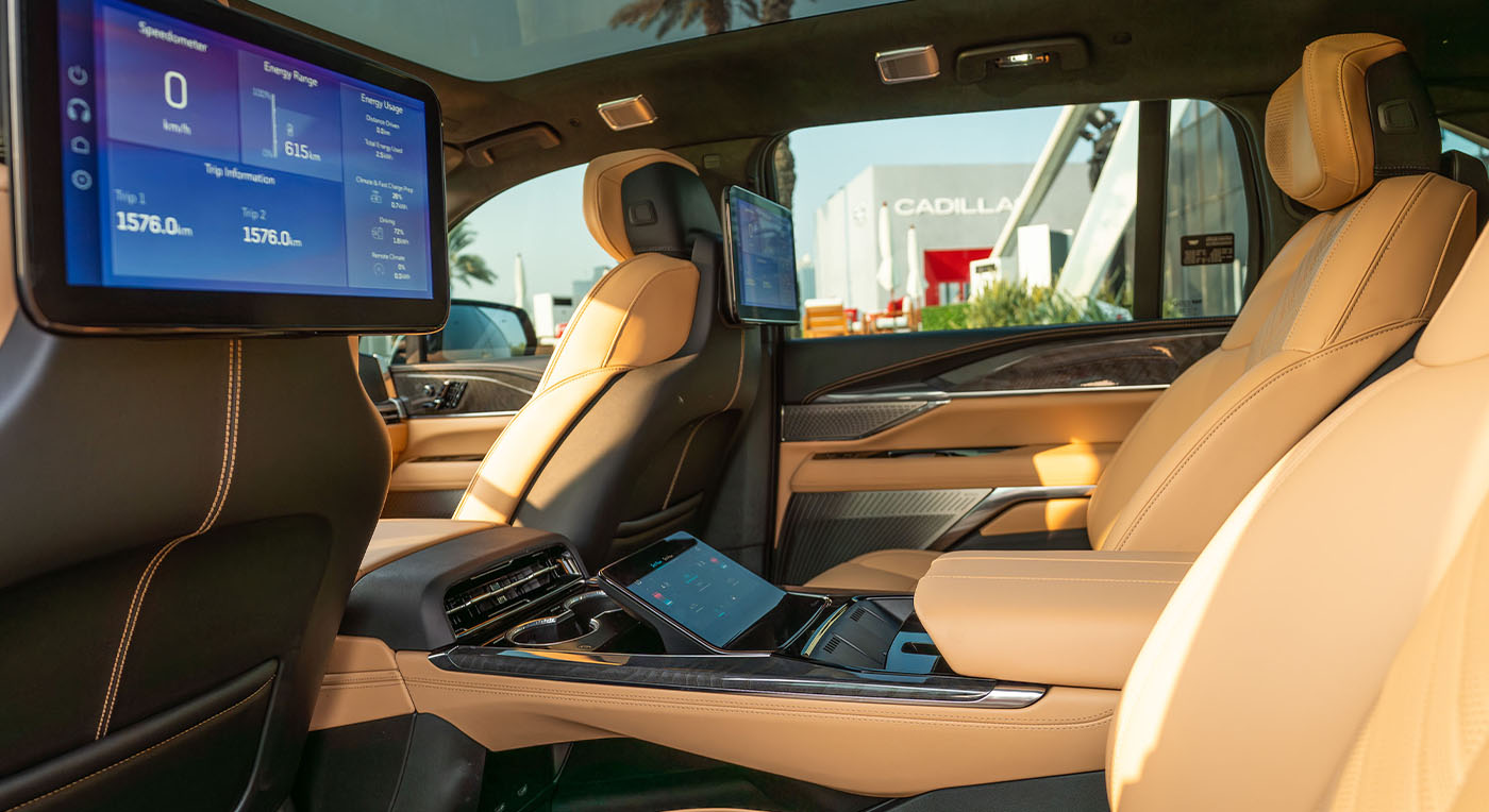 Luxurious Cadillac Escalade IQ car interior featuring beige leather seats, digital screens displaying vehicle info, and sleek design elements. Sunlit with a modern, sophisticated feel.